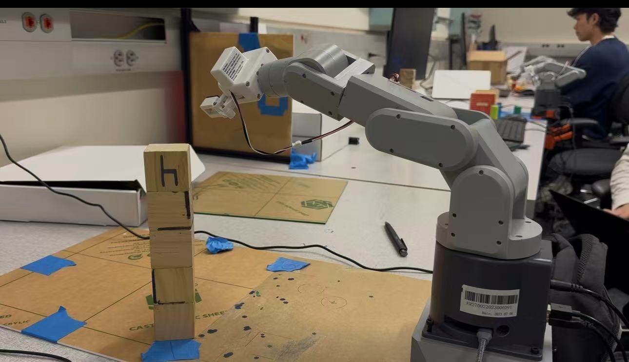 Robotic arm stacking wooden blocks during a lab demonstration.